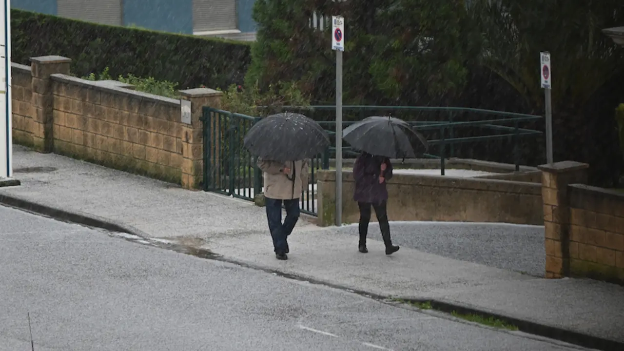 Varias personas caminan bajo una intensa granizada en la zona de Valdenoja, Santander. / HARDY