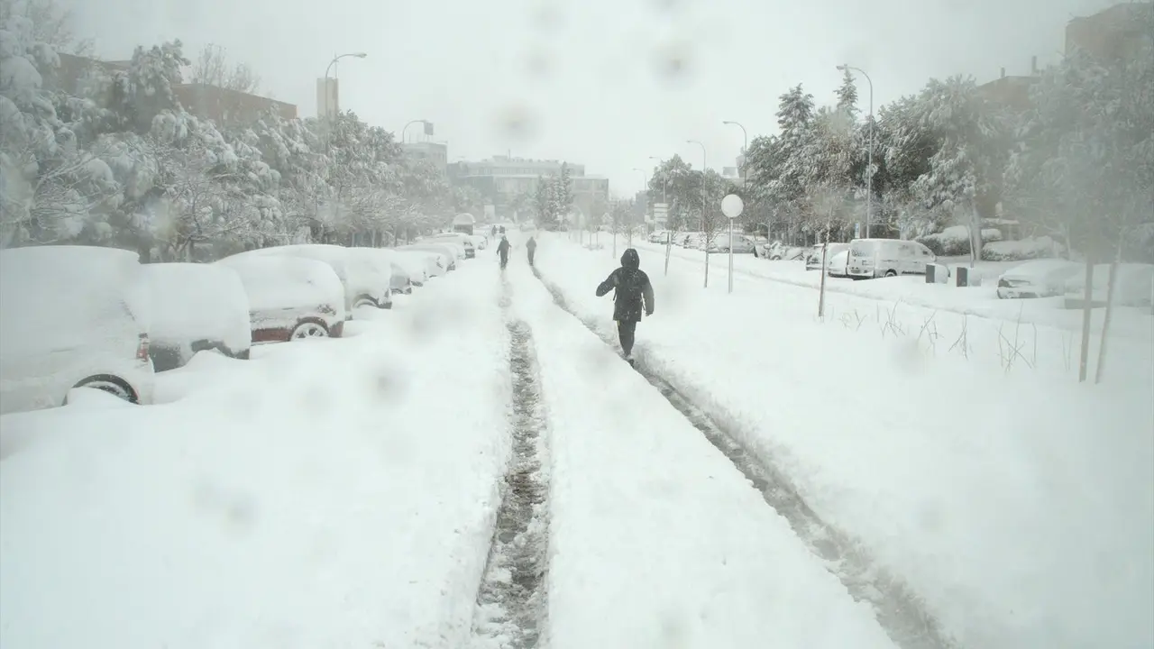 Algunas personas caminan por una calzada completamente cubierta de nieve de una calle en Alcobendas, Madrid (Espa&ntilde;a) a 9 de enero de 2021