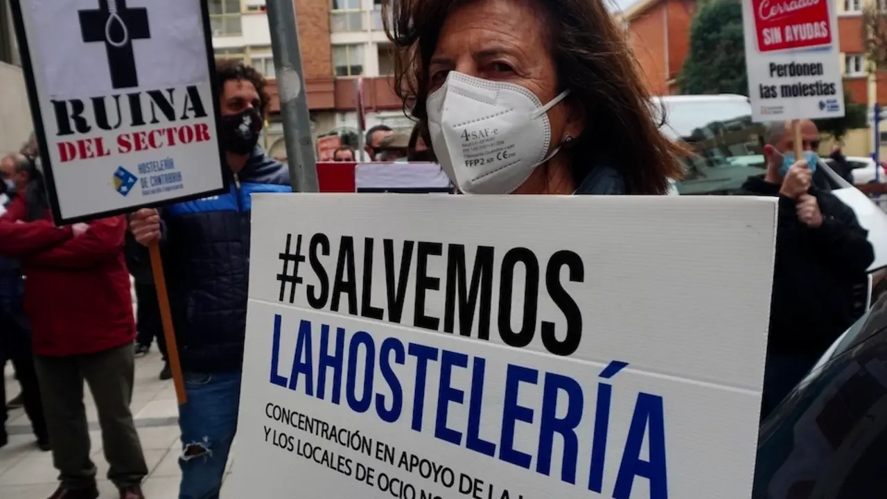 Una mujer sostiene un cartel en la manifestaci&oacute;n frente a la consejer&iacute;a de Sanidad para pedir la vuelta a la actividad de la hosteler&iacute;a. / HARDY