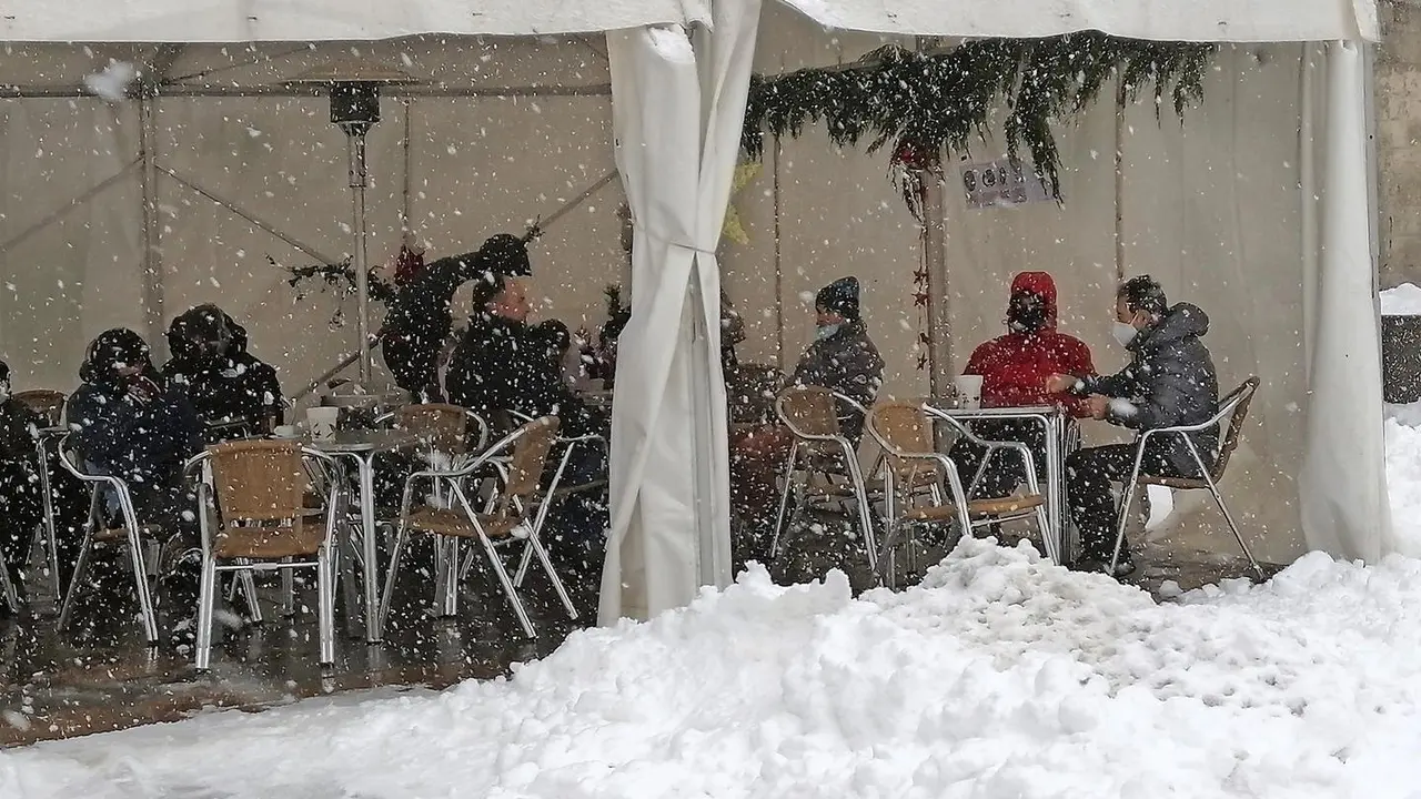 Varias personas en una terraza en la localidad de Reinosa donde la nieve cubre las principales calles. Foto: Queimadelos