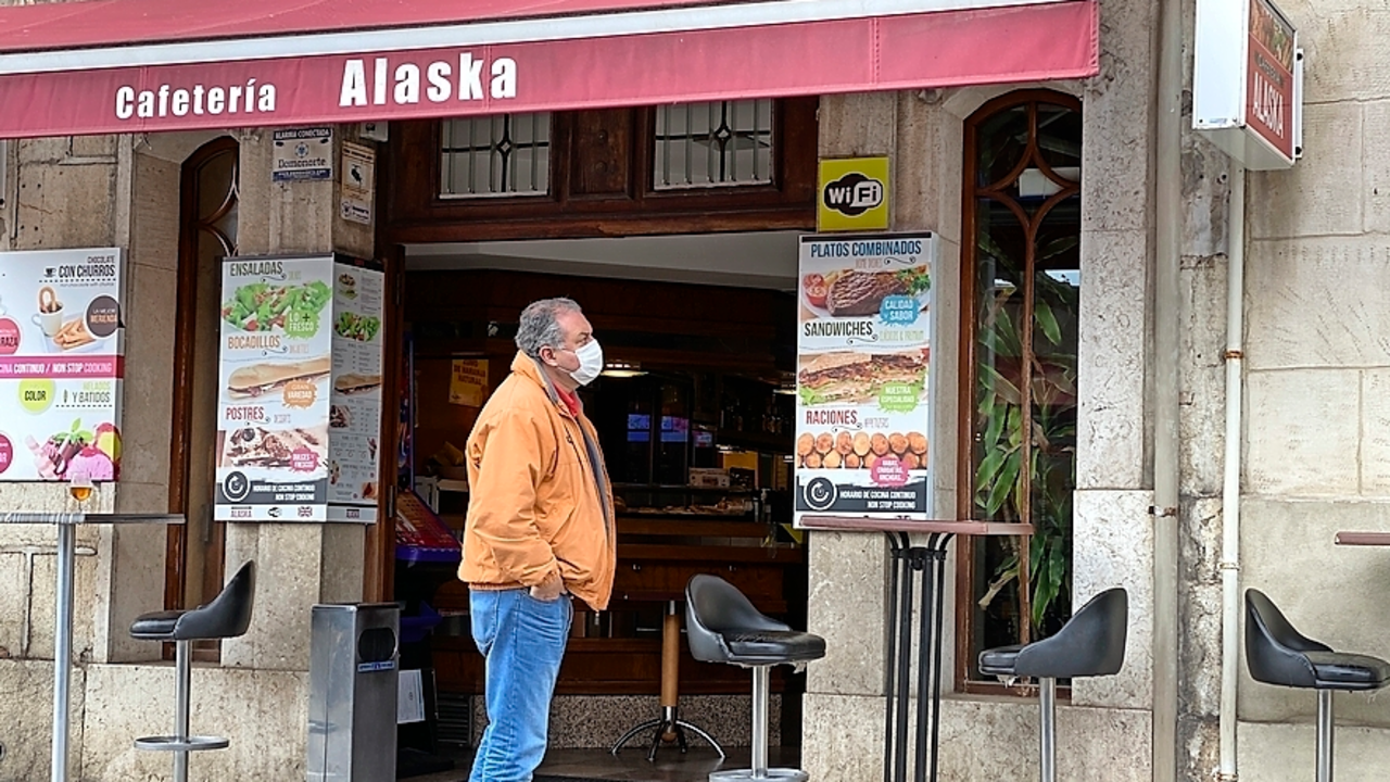 Una persona con mascarilla a la puerta de un establecimiento hostelero en el centro de Santander vac&iacute;o. / HARDY