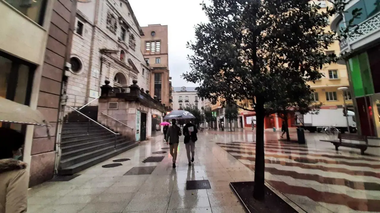 Varias personas transitan por el centro de Santander resguardados por su paraguas. / S. D&iacute;az