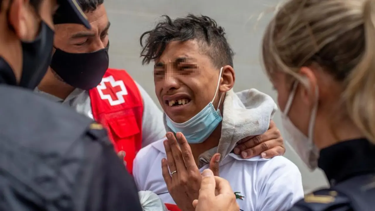 Un migrante que ten&iacute;a miedo de ser devuelto a Marruecos llora ante un voluntario de Cruz Roja y un efectivo de la Polic&iacute;a Nacional, hoy viernes en la nave de el pol&iacute;gono industrial cercano a la playa de El Tarajal en donde permanecen gran parte de los menores migrantes llegados a Ceuta. La frontera del Tarajal que separa Ceuta de Marruecos as&iacute; como el espig&oacute;n fronterizo no han registrado esta noche ni a primeras horas de la ma&ntilde;ana de este viernes intentos de entrada, de modo que no se cumplen ya dos d&iacute;as sin actividad en la zona. EFE/ Brais Lorenzo