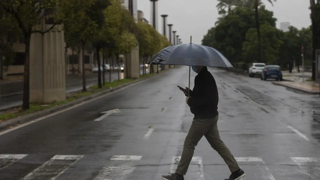 Archivo - Un hombre camina protegido de la lluvia con un paraguas