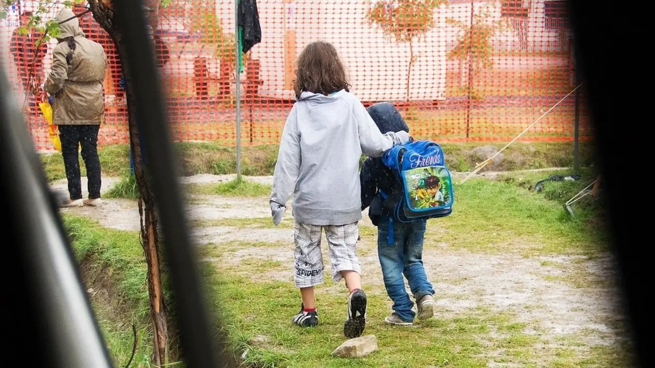 Dos ni&ntilde;os caminan bajo la lluvia en el entorno de un colegio