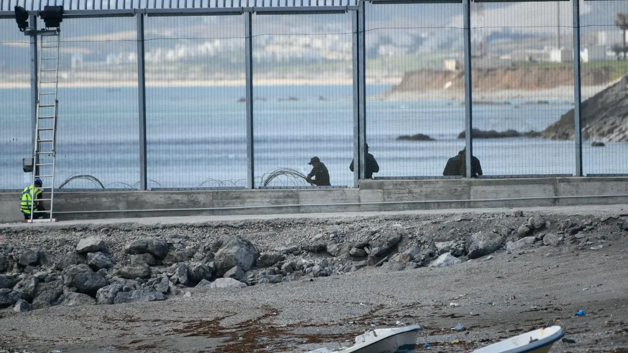 Agentes de la Gendarmer&iacute;a Real marroqu&iacute; y Fuerzas auxiliares (Mejania) levantan alambradas de concertinas en la parte inferior del vallado en el espig&oacute;n del Tarajal, a 1 de junio de 2021