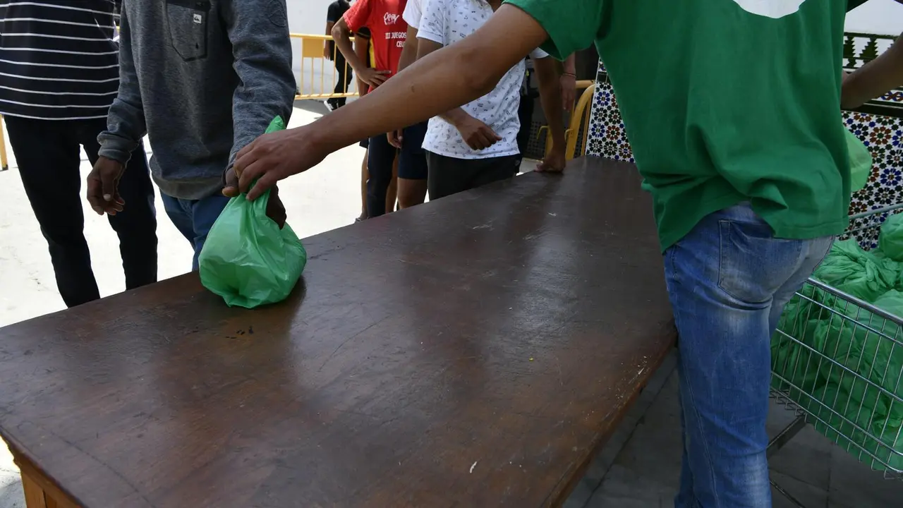 Un miembro de la asociaci&oacute;n isl&aacute;mica 'Luna Blanca' reparte una bolsa de comida a varios migrantes en Ceuta (Espa&ntilde;a), en una imagen de la pasada semana