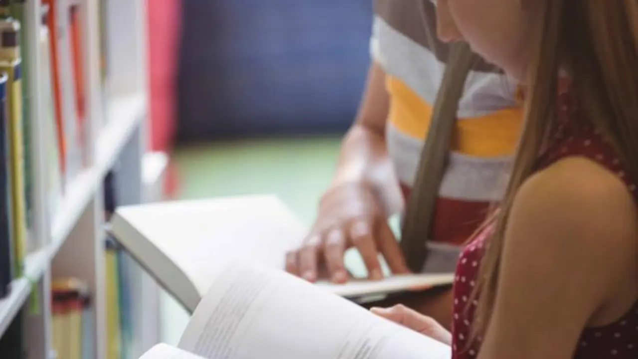 Attentive classmates reading book in library at school