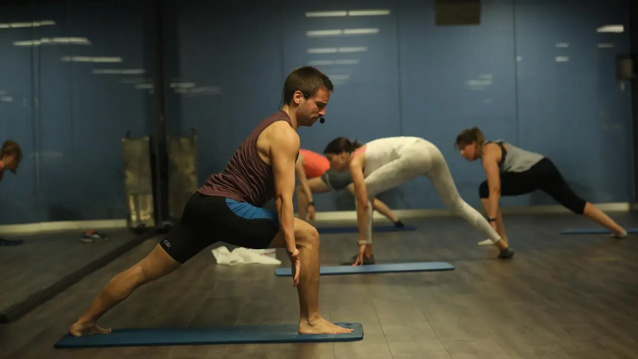 Archivo - Un entrenador imparte clase a varias personas en una clase de Body Balance en un gimnasio de Madrid.