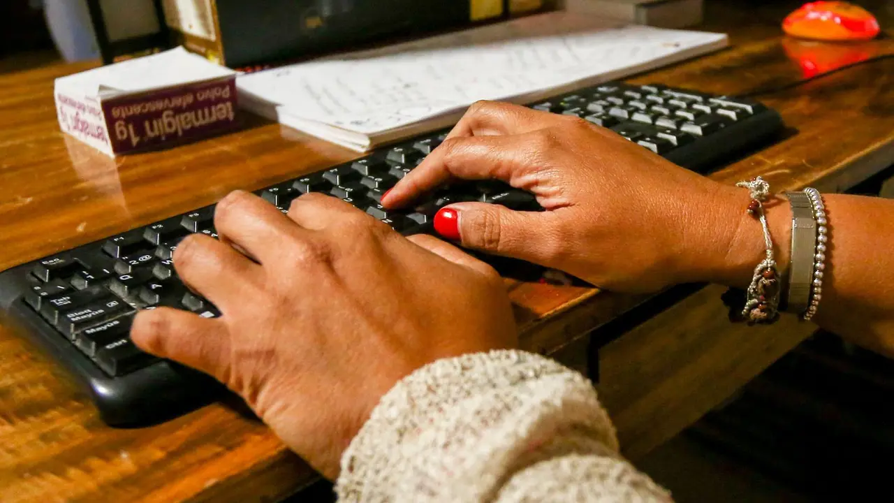 Archivo - Unas manos de mujer escriben en el teclado de un ordenador, sobre una mesa de madera.