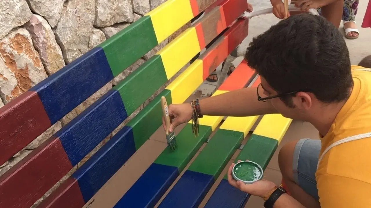 Archivo - Joven pintando un banco de los colores LGTBI