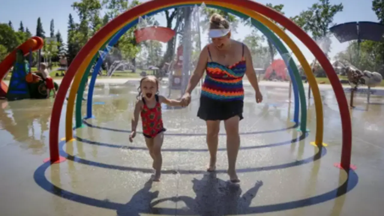 Una madre y su hija corren entre aspersores para tratar de vencer el calor en un parque. - Jeff Mcintosh/The Canadian Press / DPA