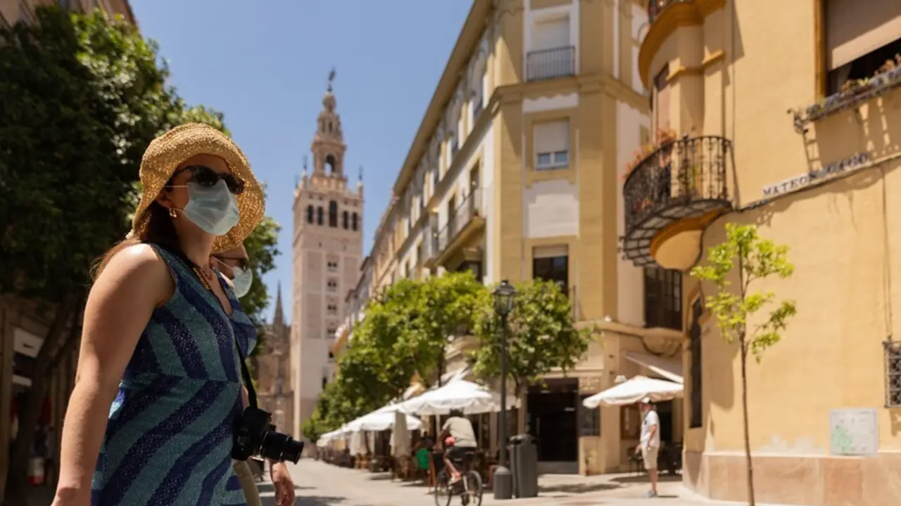 Turistas pasean por el centro de Sevilla provistos de gorras, abanicos y botellas de agua 