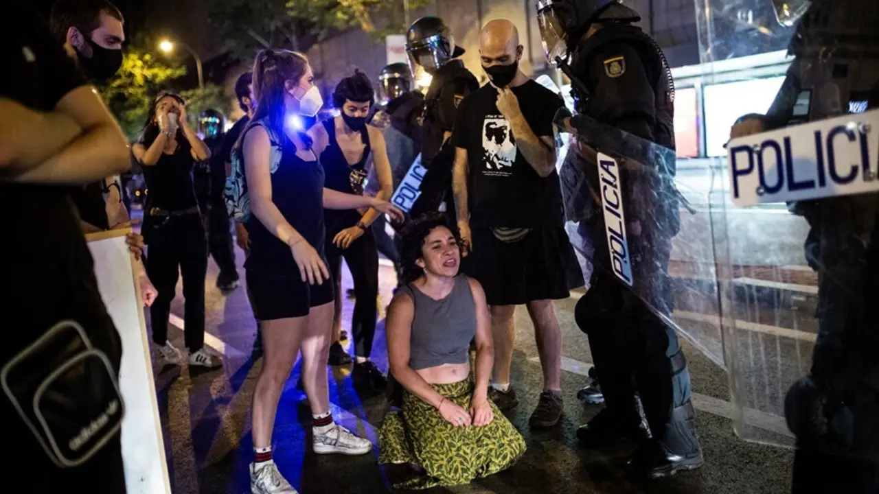 Una joven arrodillada frente a antidisturbios de la Polic&iacute;a Nacional en el barrio de Arg&uuml;elles tras la concentraci&oacute;n por el asesinato del joven Samuel a 5 de julio de 2021 en Madrid (Espa&ntilde;a). 