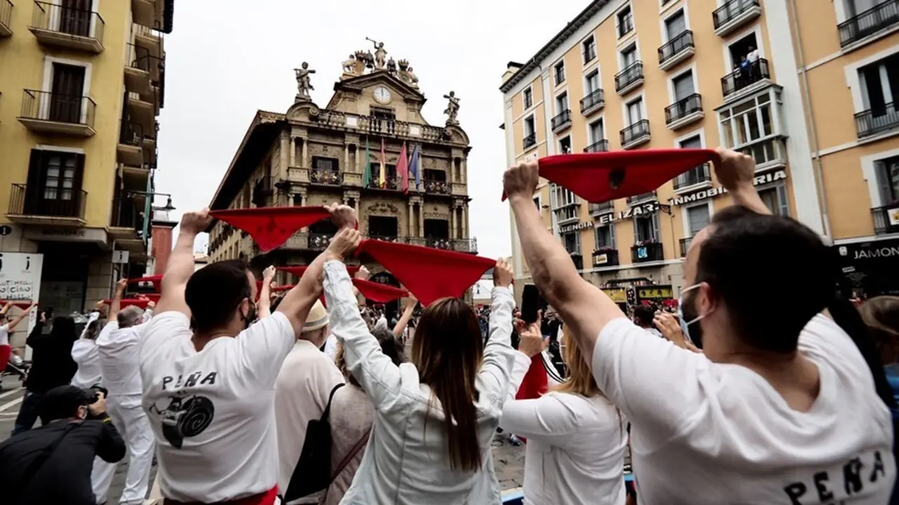 Varias personas levantan los pa&ntilde;uelos rojos a las 12 del mediod&iacute;a en la plaza del Ayuntamiento de Pamplona, momento en que habr&iacute;a tenido lugar el tradicional chupinazo de San Ferm&iacute;n, suspendidos por segundo a&ntilde;o por la pandemia