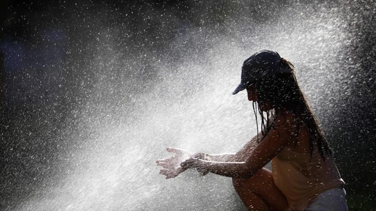Una joven trata de mitigar los altas temperaturas que se alcanzar&aacute;n este domingo en C&oacute;rdoba, superiores a 40 grados, refresc&aacute;ndose con los aspersores de riego de un parque. EFE/Salas