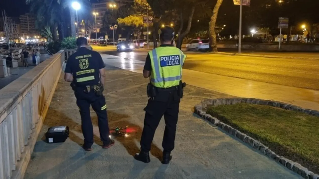 Un agente de la Polic&iacute;a Local y un agente de la direcci&oacute;n General de Emergencias del Govern junto al dron utilizado en el dispositivo antibotell&oacute;n.