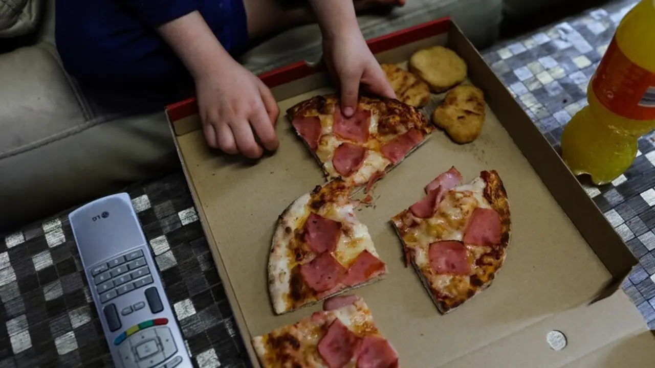 Archivo - Un ni&ntilde;o come pizza del men&uacute; infantil de Telepizza mientras ve la televisi&oacute;n en su casa