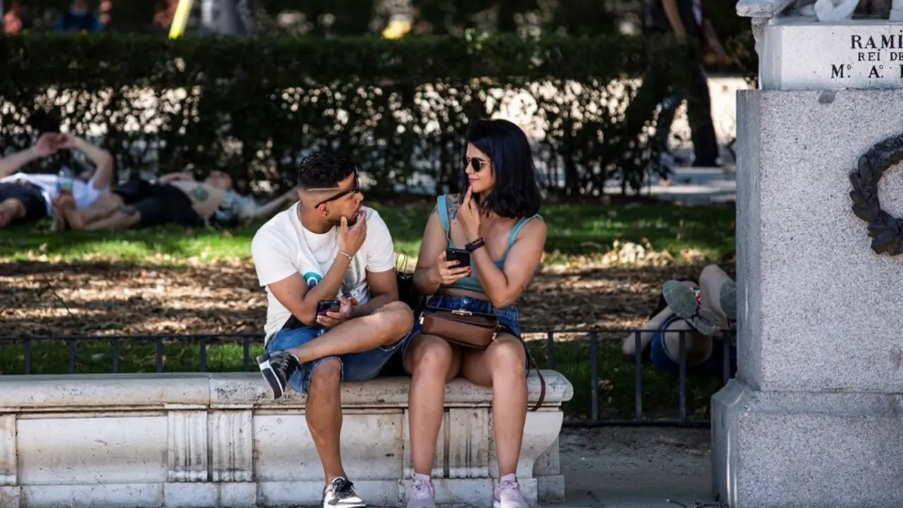 Dos personas sin mascarilla, sentadas en un banco de la Plaza de Oriente