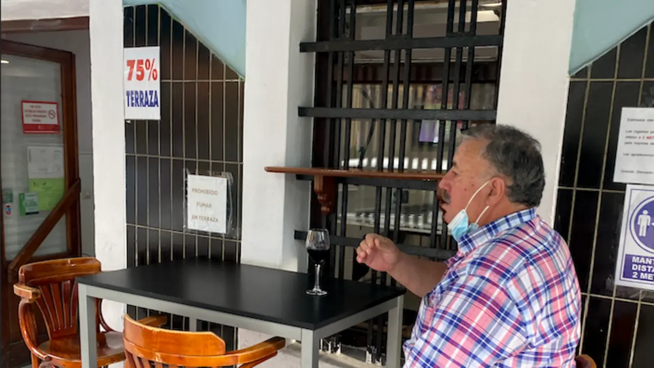 Un hombre toma un vino en una terraza en Santander bajo el cartel de 75% de aforno.  / ALERTA