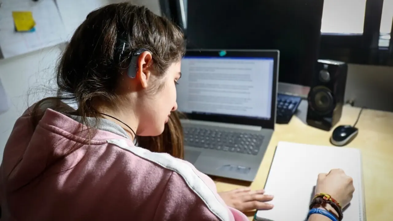 Archivo - Una joven usuaria de aud&iacute;fonos estudia en su habitaci&oacute;n