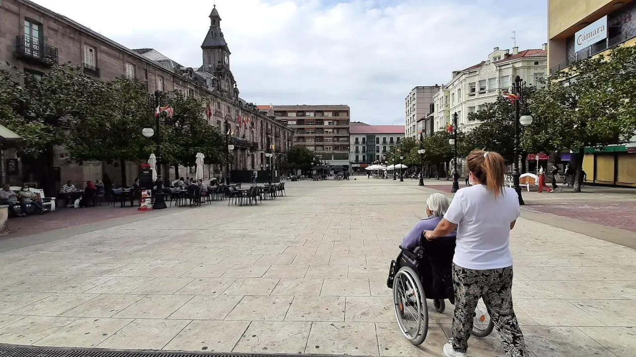 Una persona camina con una persona con movilidad reducida por la plaza del Ayuntamiento de Torrelavega. / S. D&iacute;az