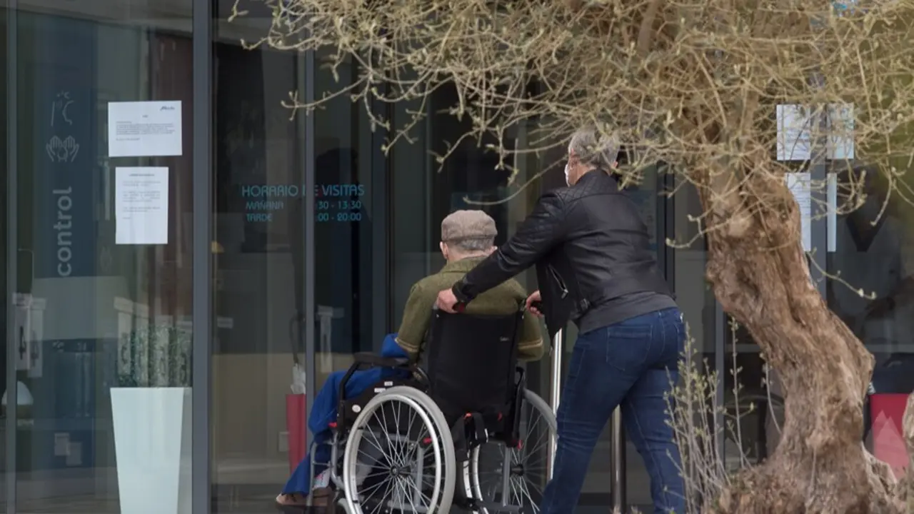 Archivo - Una mujer pasea junto a un anciano en silla de ruedas hacia una residencia en Lugo.