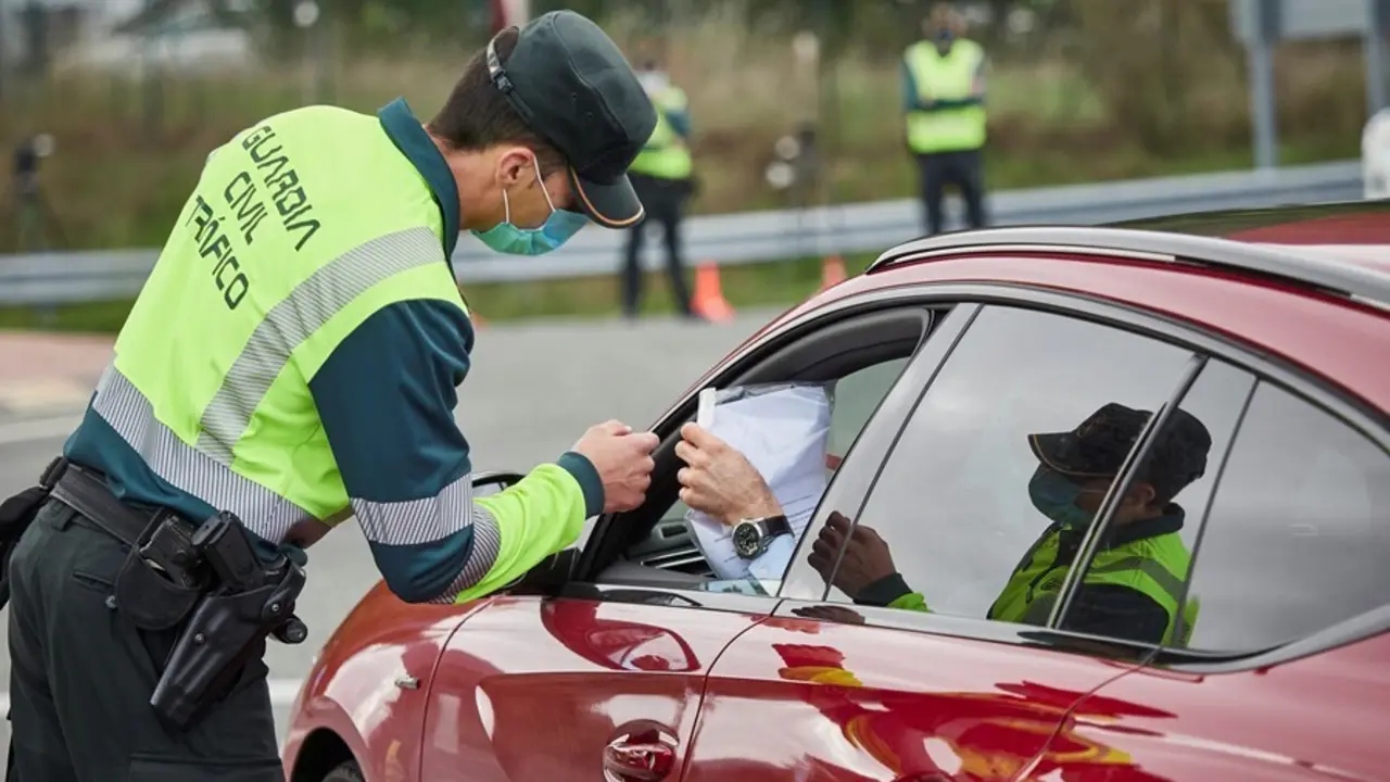 Archivo - Un agente de la Guardia Civil de Tr&aacute;fico comprueba la documentaci&oacute;n de un conductor en un control policial, en una imagen de archivo.