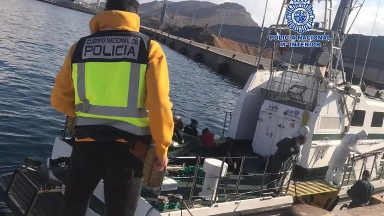 Un agente observa un barco en el que se encuentran varias personas inmigrantes