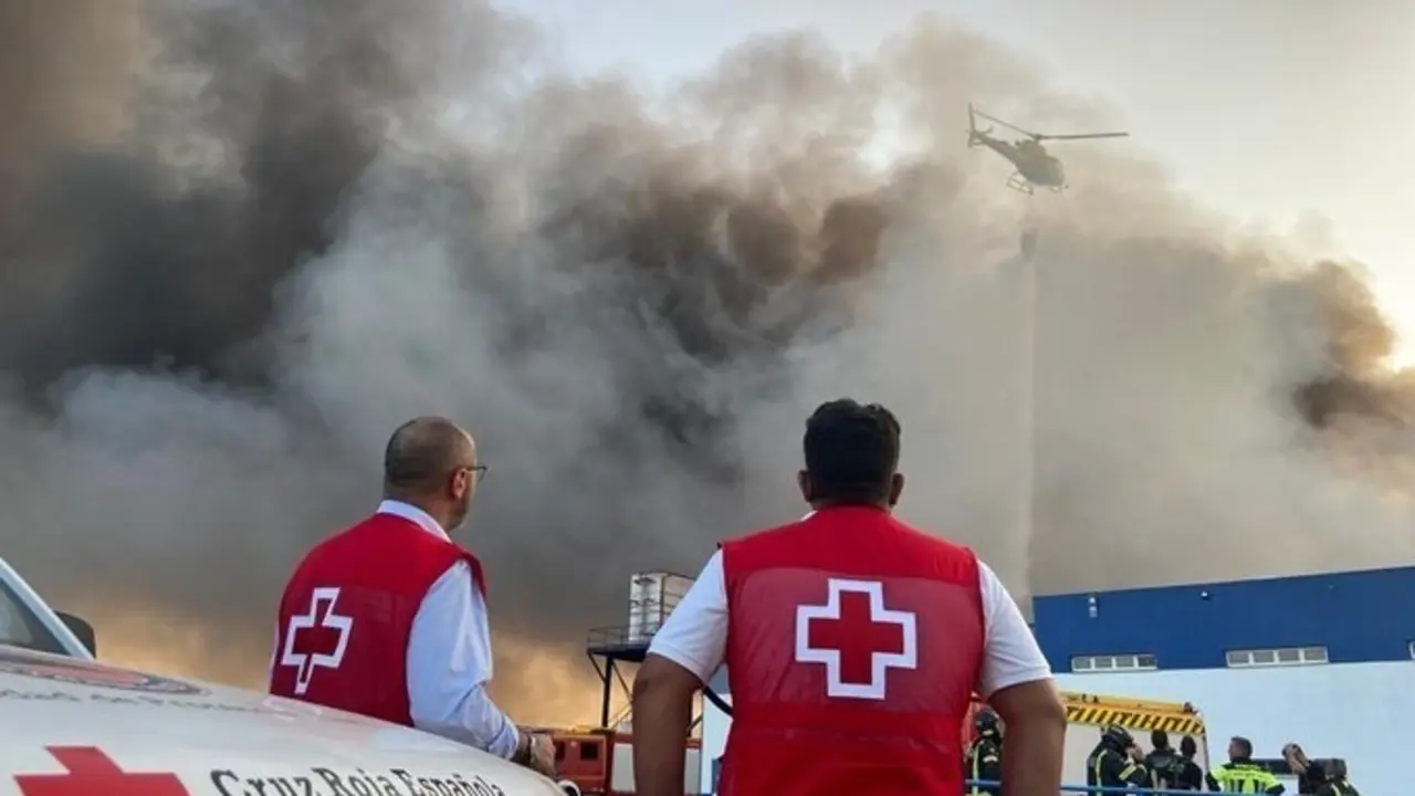 Voluntarios de Cruz Roja contemplan la columna de humo en la central hostofrut&iacute;cola de El Escobar.