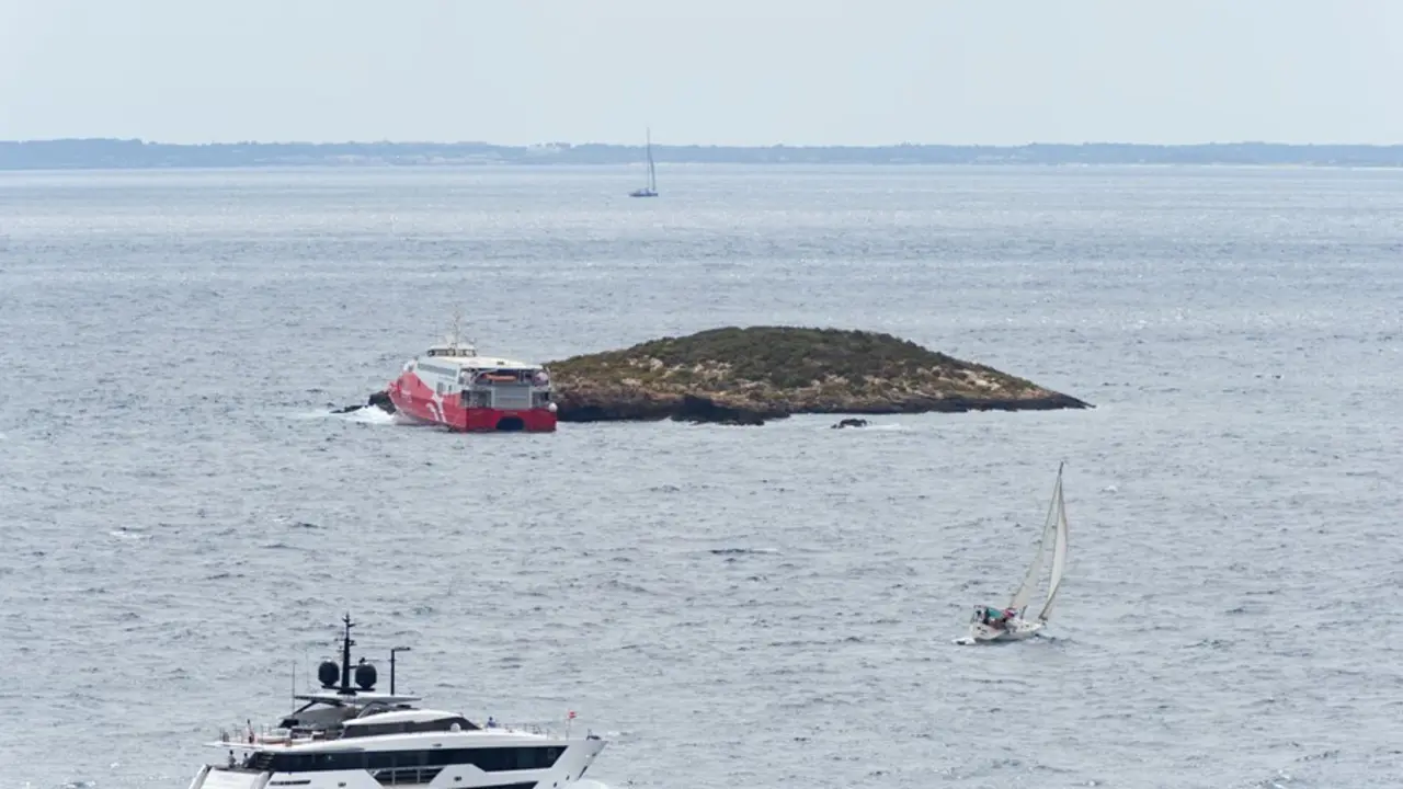 Un barco y un velero pasan cerca del ferry 'San Gwann' de la naviera FRS encallado en el islote norte de Es Malvins, entre Ibiza y Formentera. 