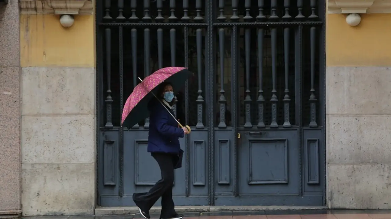 Archivo - Una mujer pasa frente a una puerta en la capital en un d&iacute;a de lluvia  