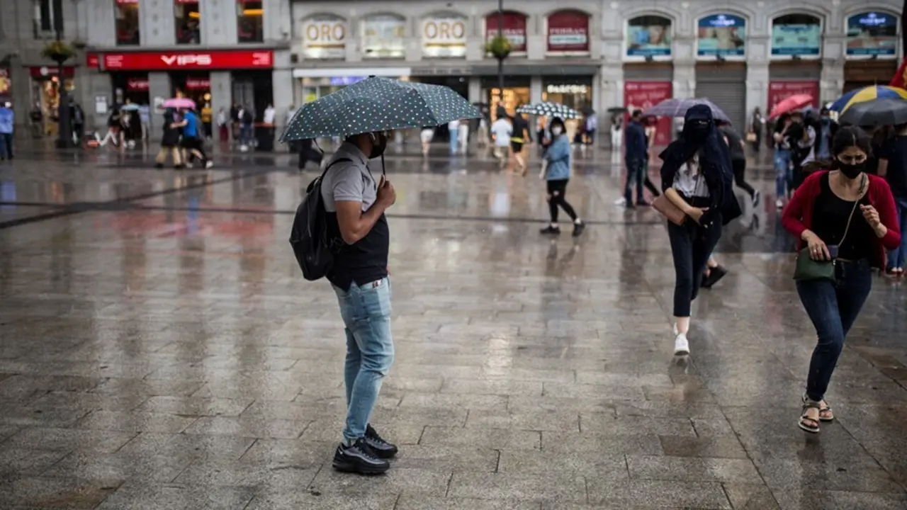 Archivo - Ciudadanos se resguardan de la lluvia durante una manifestaci&oacute;n contra la subida de la luz en la Puerta del Sol