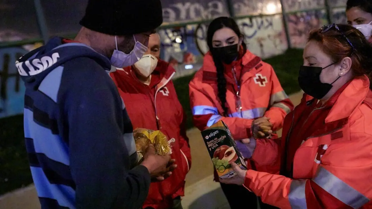 Archivo - Varios trabajadores de Cruz Roja ofrecen comida a un hombre sin hogar