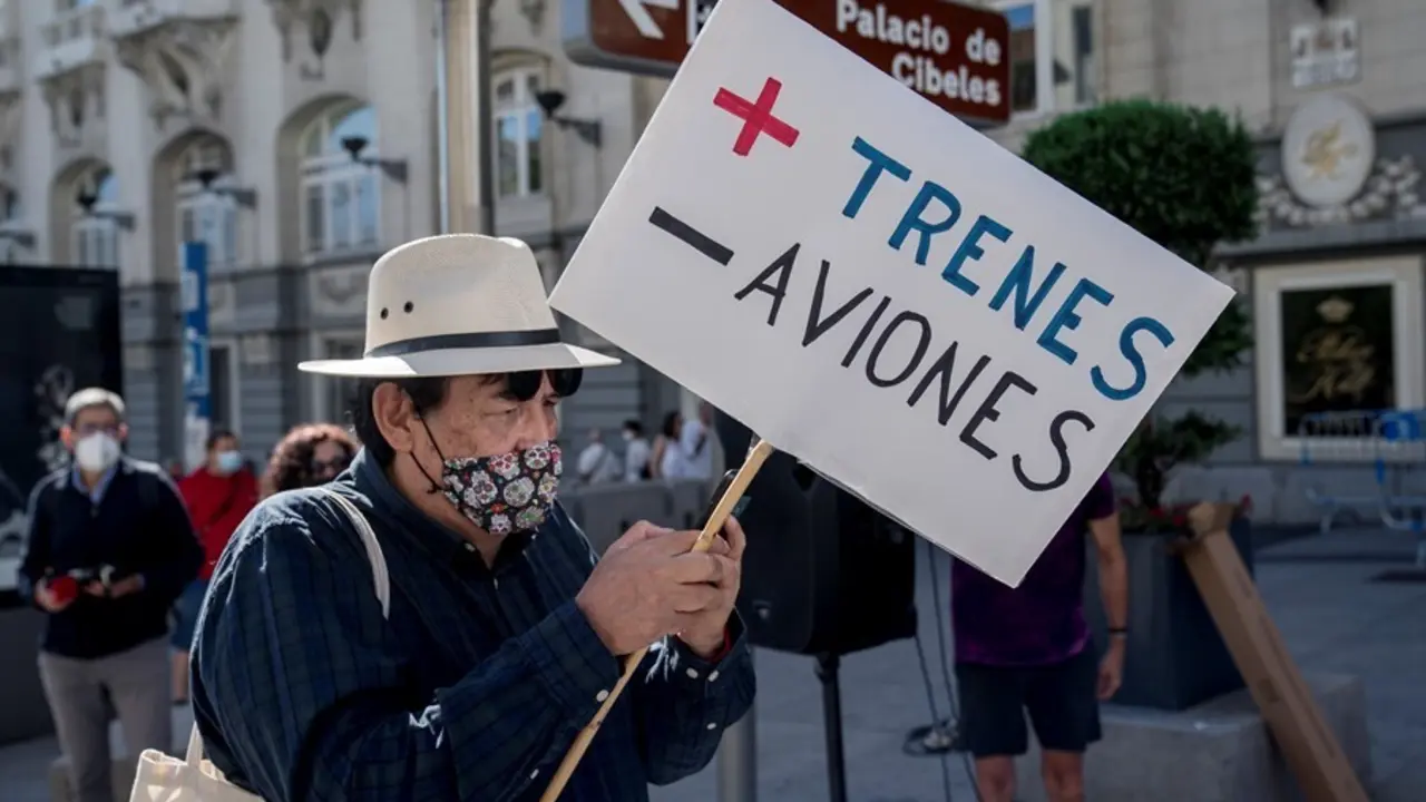 Una mujer sostiene una pancarta donde se lee "M&aacute;s trenes, menos aviones", en una concentraci&oacute;n contra la ampliaci&oacute;n del aeropuerto Adolfo Su&aacute;rez Madrid-Barajas.