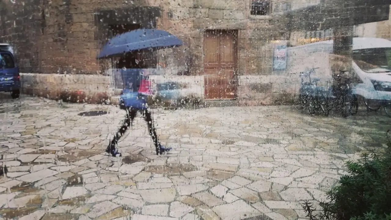 Archivo - Una mujer pasea por el centro de Palma con un paraguas, vista a trav&eacute;s de un cristal con gotas de lluvia.