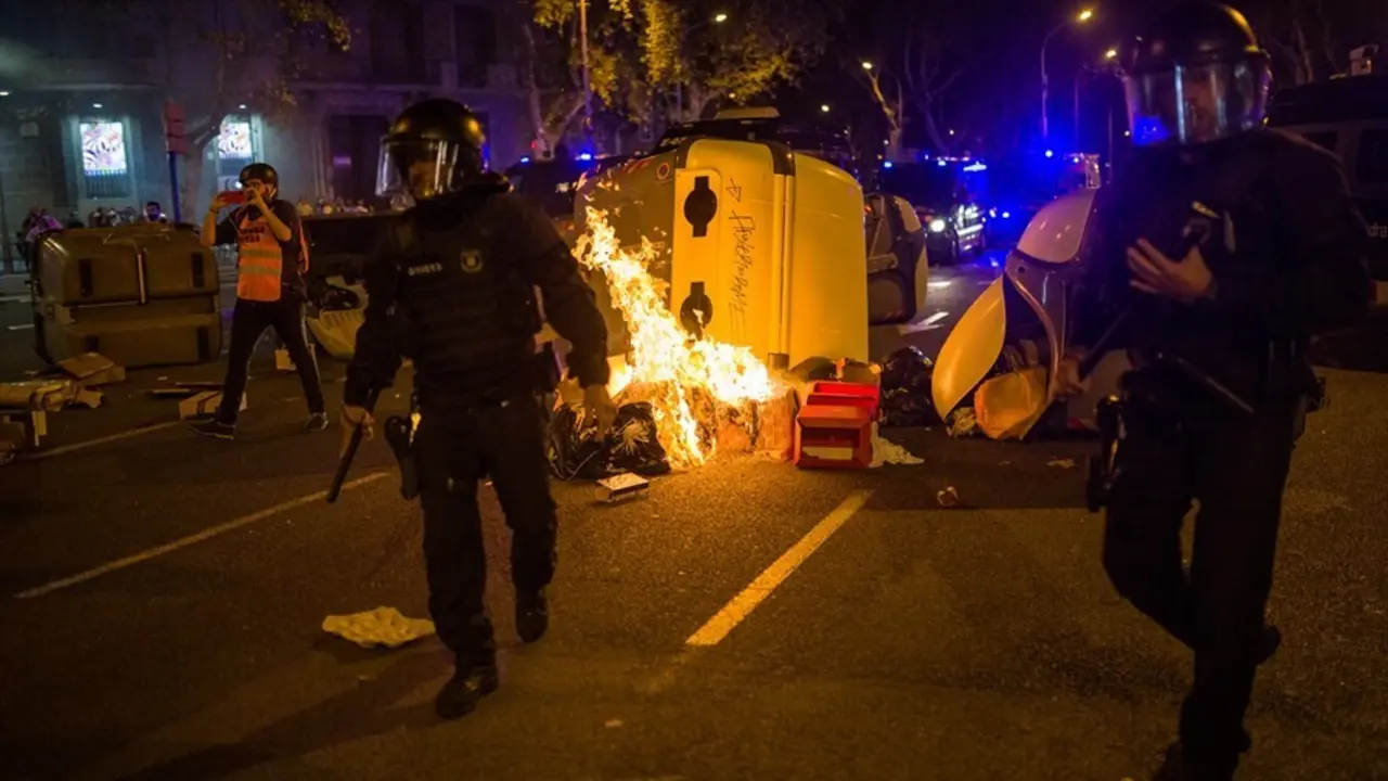 Varios mossos antidisturbios pasan delante de un contenedor quemado en la plaza Urquinaona durante una manifestaci&oacute;n por el refer&eacute;ndum del 1-O en Catalunya, a 1 de octubre de 2021, en Barcelona