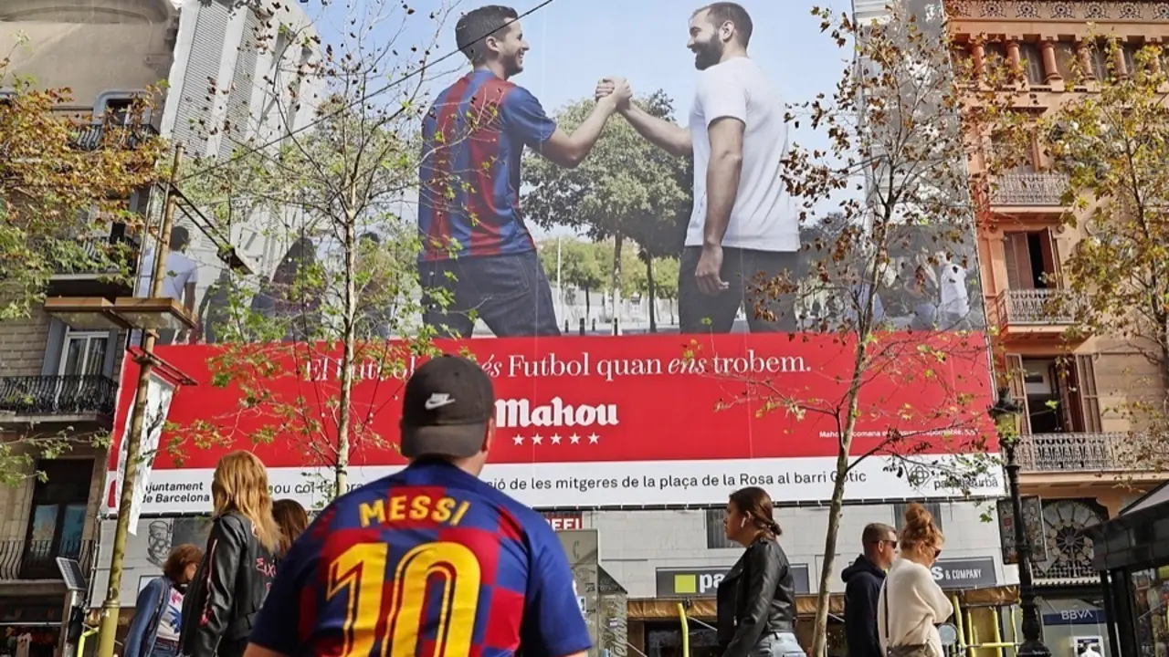 Un joven con la camiseta de Messi ante una pancarta de publicidad del cl&aacute;sico Bar&ccedil;a-Madrid, que se juega el domingo, ayer en las Ramblas de Barcelona. / Alejandro Garc&iacute;a