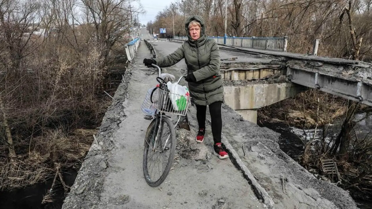 Una mujer pasa con su bicicleta por los restos del puente principal de la ciudad de Malyn, destruido tras el bombardeo de la aviaci&oacute;n rusa, en Malyn, Ucrania, el 12 de marzo de 2022. EFE/EPA/MIGUEL A. LOPES