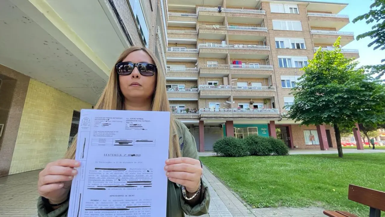 Elina en la plaza del barrio donde se ubica su vivienda, mostrando la sentencia que obliga a estas personas a salir de su casa. / alerta