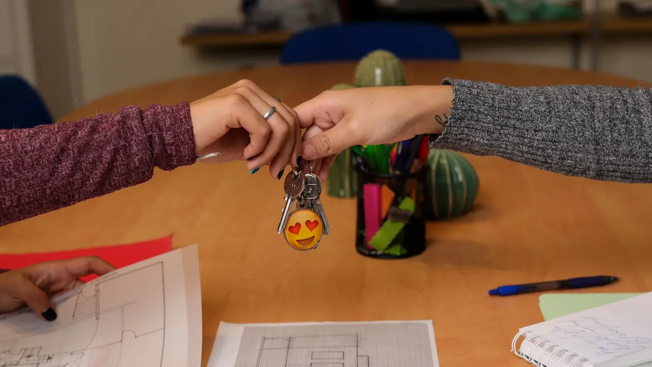 Dos chicas se dan unas llaves de una vivienda. Encima de la mesa hay varios planos sobre viviendas y material de escritura. / Jes&uacute;s Hell&iacute;n