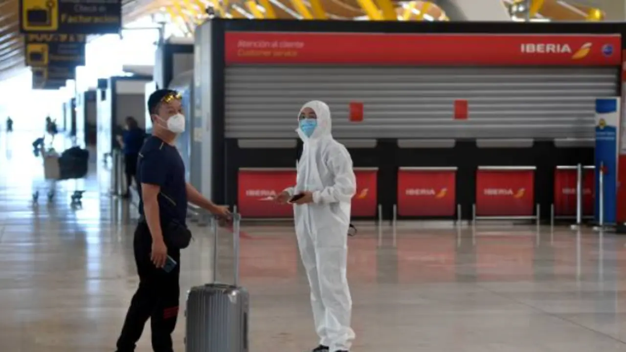 Un pasajero ataviado con un traje de protecci&oacute;n espera junto a un familiar tras facturar un vuelo con destino a Pek&iacute;n en el aeropuerto de Barajas. / E.P.