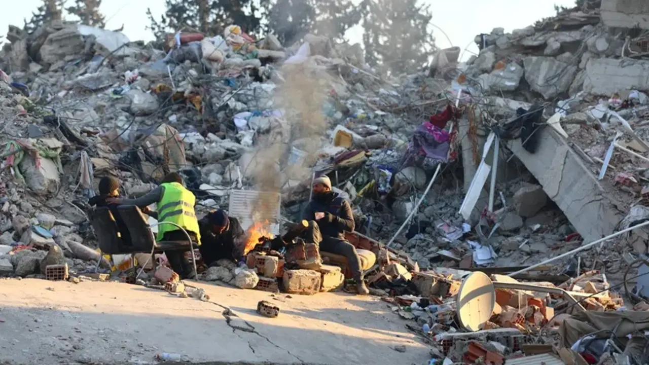 Familiares de personas desaparecidas se calientan alrededor de una hoguera encendida sobre los escombros de un edificio derrumbado por el terremoto. EFE / Tolga Bozoglu