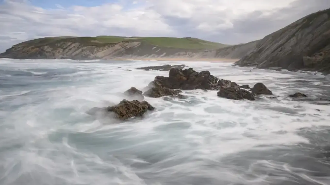 Una ola rompe sobre las rocas en la playa de Tagle