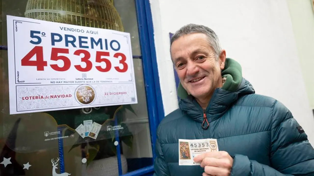 TORRELAVEGA, 22/12/2023.- Un agraciado con un d&eacute;cimo del n&uacute;mero 45.353, uno de los quintos premios del sorteo extraordinario de la Loter&iacute;a de Navidad, posa ante la administraci&oacute;n n&ordm; 6 de Torrelavega este viernes. EFE/ Pedro Puente Hoyos