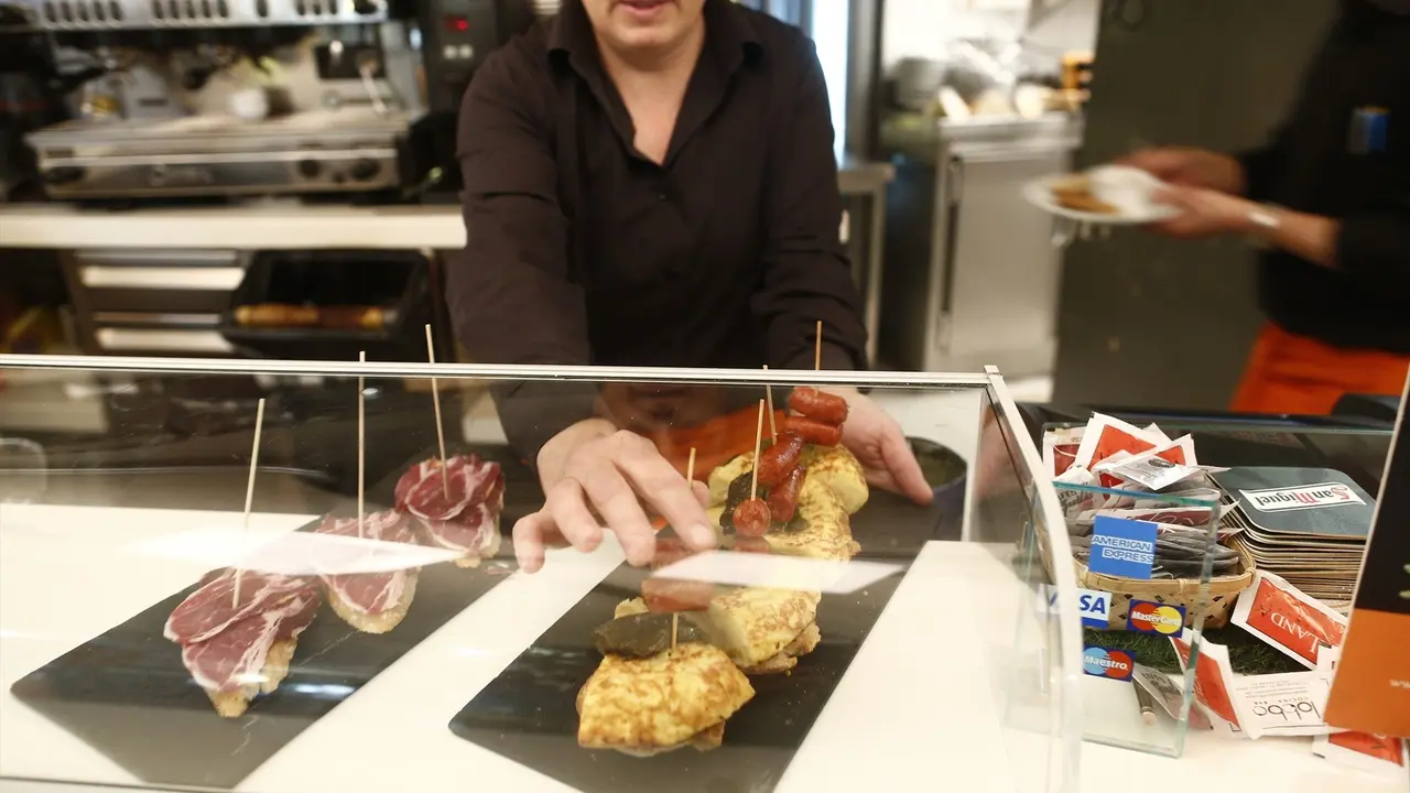 Una camarera coloca unos pinchos en la barra del bar. / EP