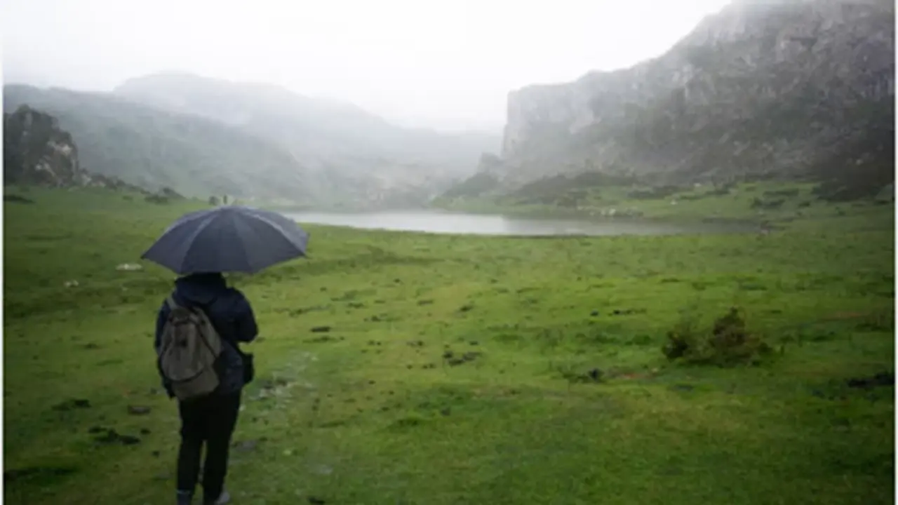 Una persona con un paraguas bajo la lluvia mirando un paisaje. / A.S.