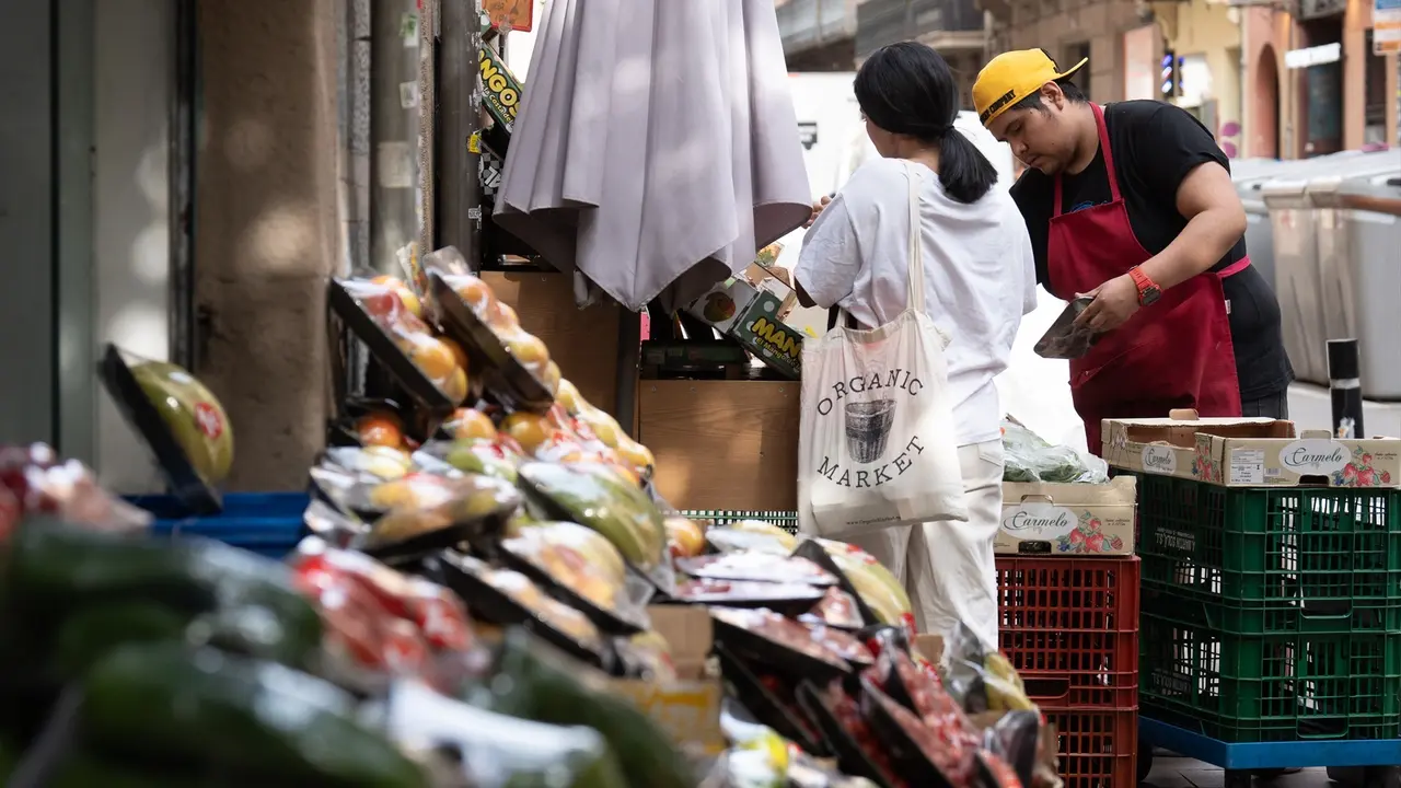 Varias frutas expuestas en el exterior de una fruter&iacute;a mientras un dependiente atiende a un cliente. /  David Zorrakino