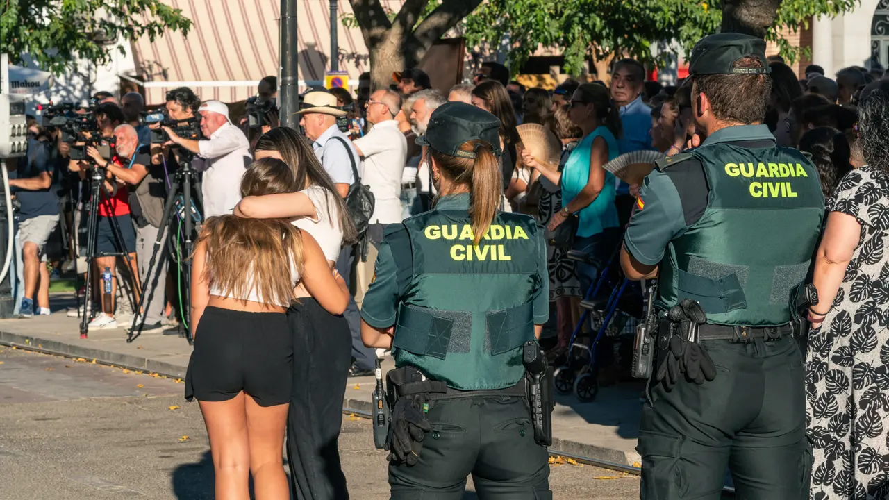 Dos agentes de la Guardia Civil observan a dos chicas abrazadas durante el minuto de silencio por el asesinato de un menor. / Juan Moreno