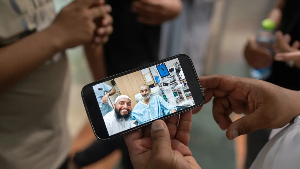 El reh&eacute;n israel&iacute; liberado Kaid Alkadi fotografiado en el interior de la sala de urgencias con un tel&eacute;fono m&oacute;vil mientras sus familiares se re&uacute;nen frente al Centro M&eacute;dico de Beersheva, en el sur de Israel. / Ilia yefimovich
